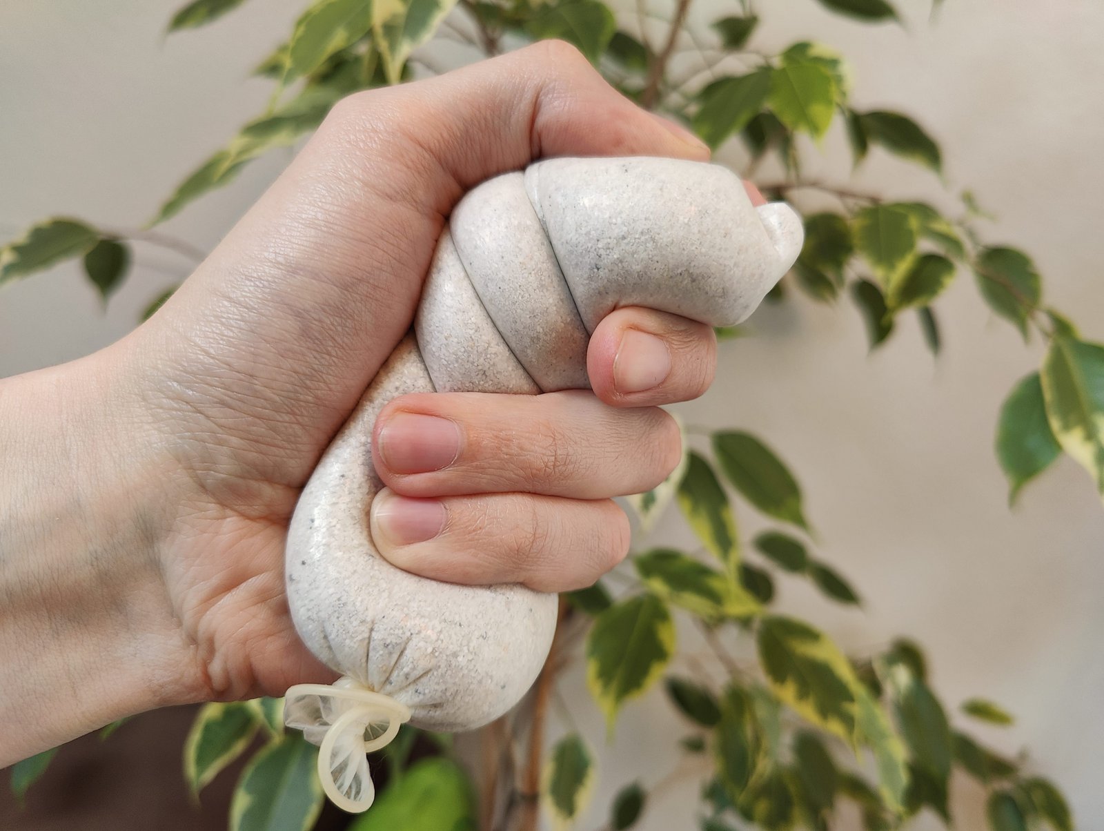 Przeterminowana prezerwatywa wypełniona piaskiem w dłoni osoby używającej jej jako piłki antystresowej.